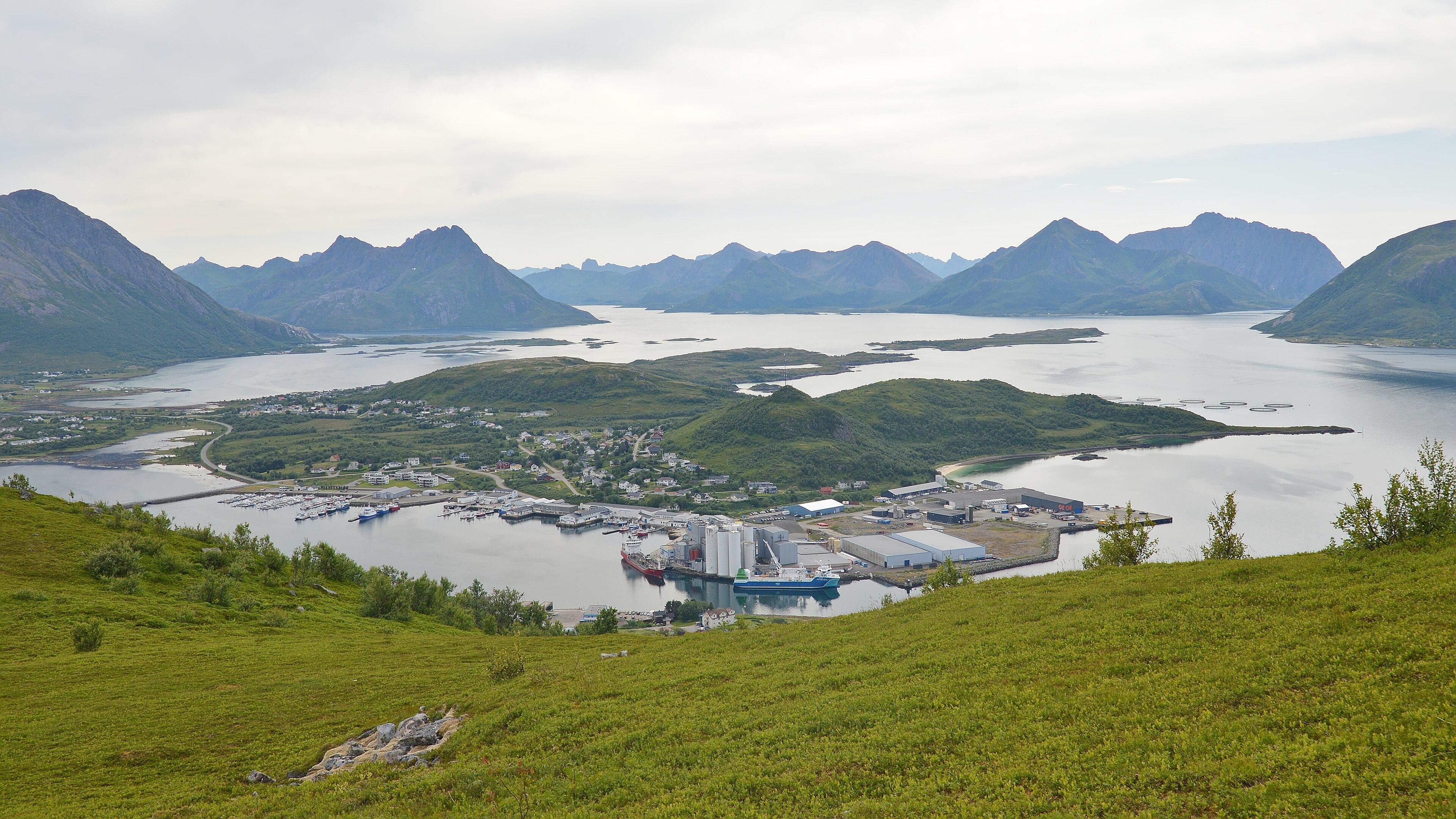 A photo looking down from a mountain at a peninsula. There are mountains in the distance. The sky is filled with clouds.