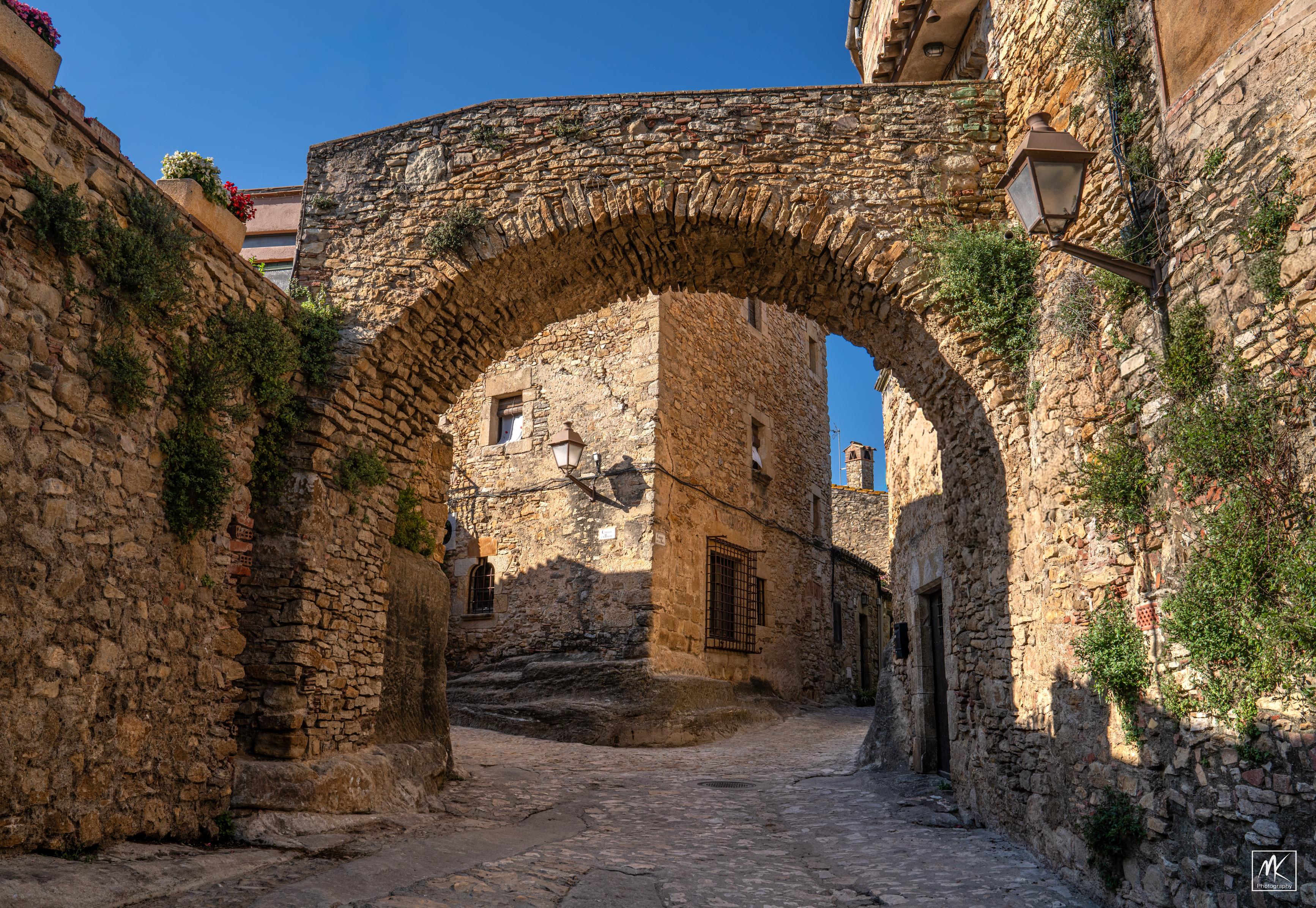 Color photo of a stone arch over a cobblestone street in a medieval Catalonian town.