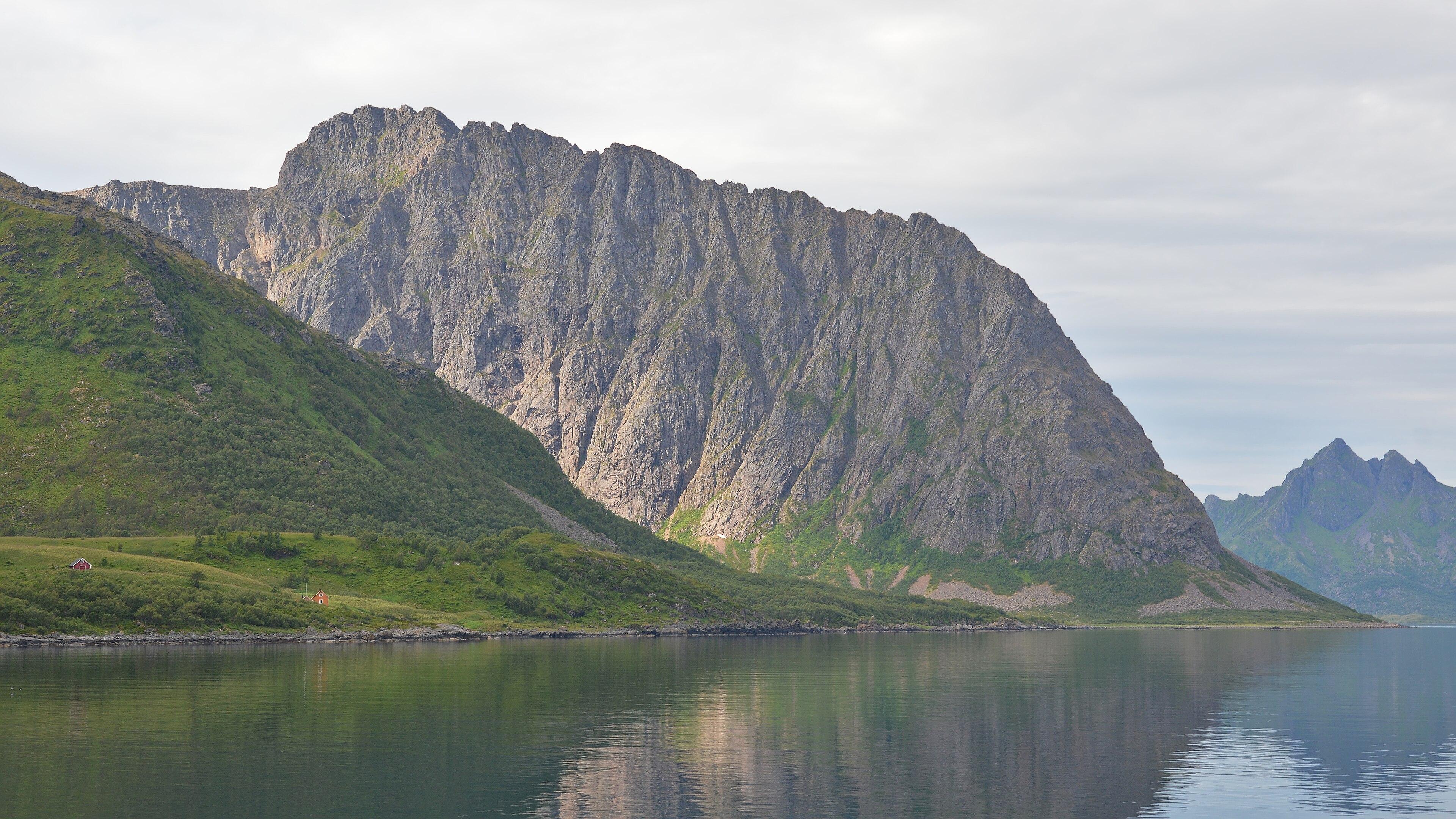 A photo of a jagged mountain going into water. The sky is filled with clouds.