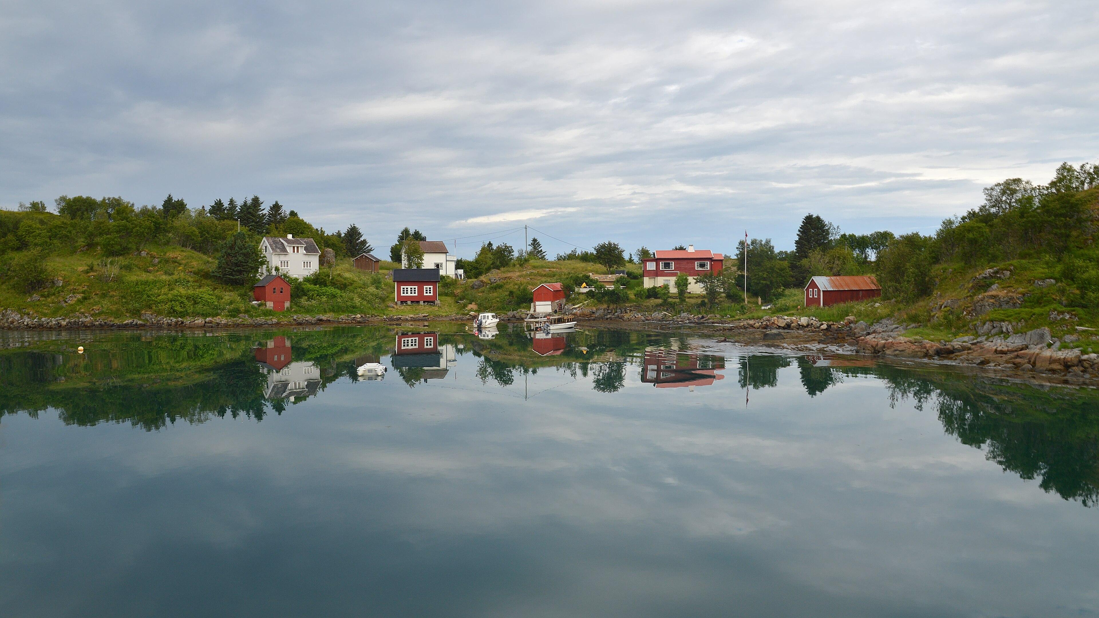 A photo of part of a small village on the water. The building are red and white. The sky is filled with clouds.