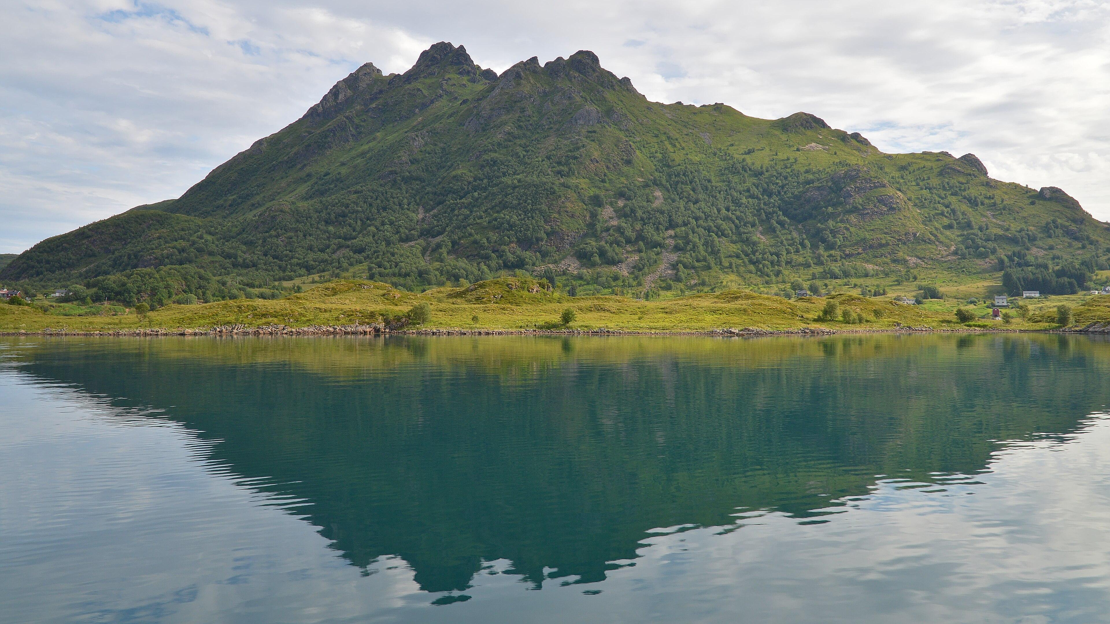 A photo of a green mountainous island with jagged peaks. The sky is filled with clouds..
