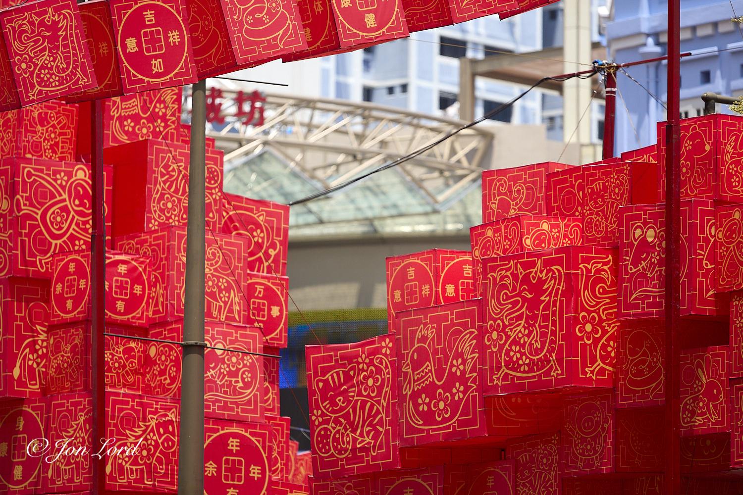 This is a colour street photo in landscape format of countless patterned red cubes suspended over a city street. New Bridge Road, Singapore (2013).

Dominating nearly the entire photo are these multiple, bright red cubes. Each with a gold animal or Chinese character printed on the sides. The camera is located above the street and at the same level as the cubes with most of them being only a few metres away. Each cube is about one metre in all dimensions with them grouped together in their hundreds and suspended from poles or street lights high above the street. The animal pictures repeat numerous times: these include the traditional and compulsory Chinese dragon, Rabbit, Mouse and since it was the year of the Snake, a Snake. A few electric cables can be seen overhead suggesting that the cubes are lit after dark. The only area without cubes is a narrow portion of the photo stretching from the centre of the image diagonally upwards and into the upper right corner where there is what migh
