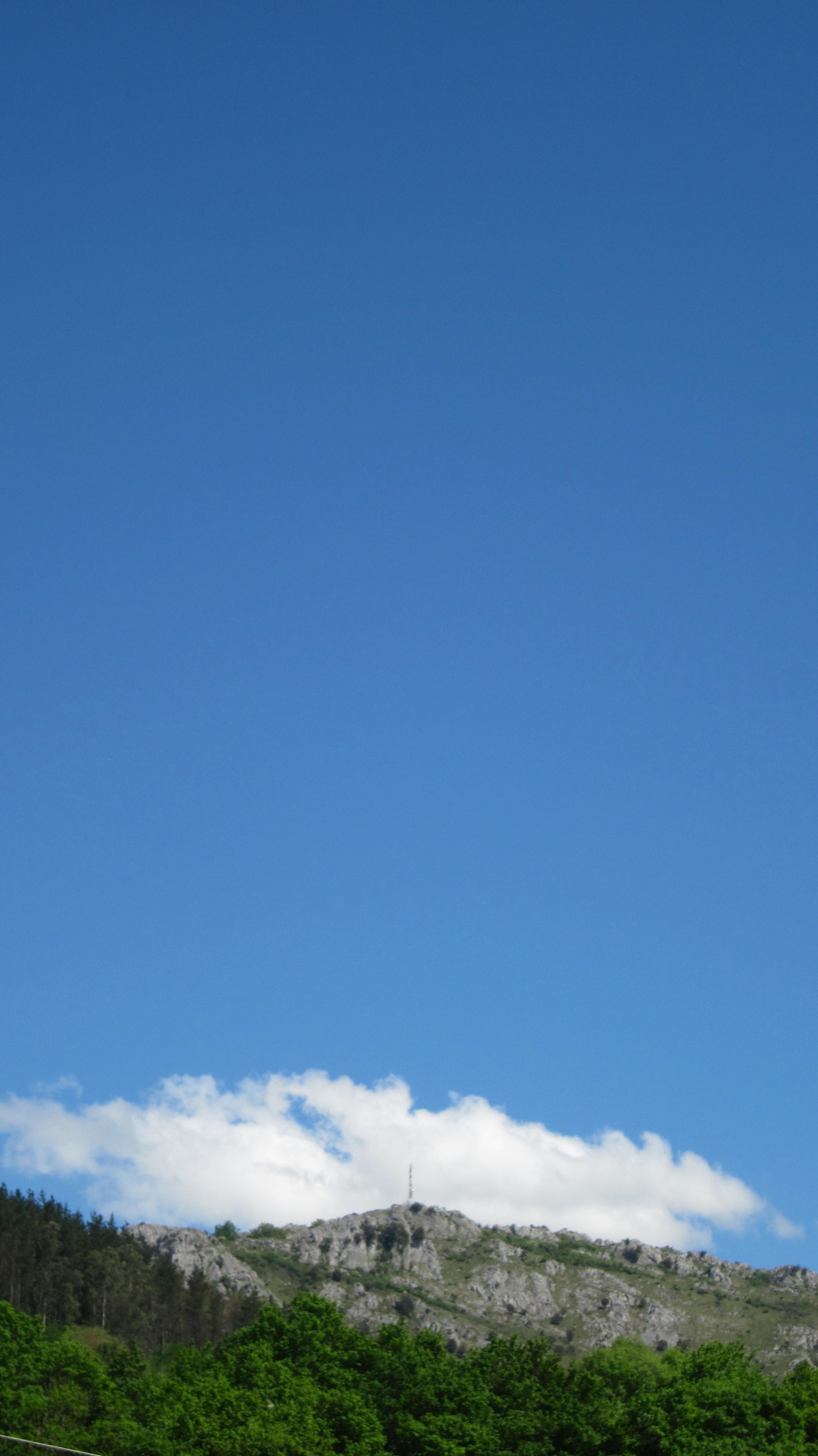 Fotografía en color de una montaña bajo el cielo azul y una gran nube