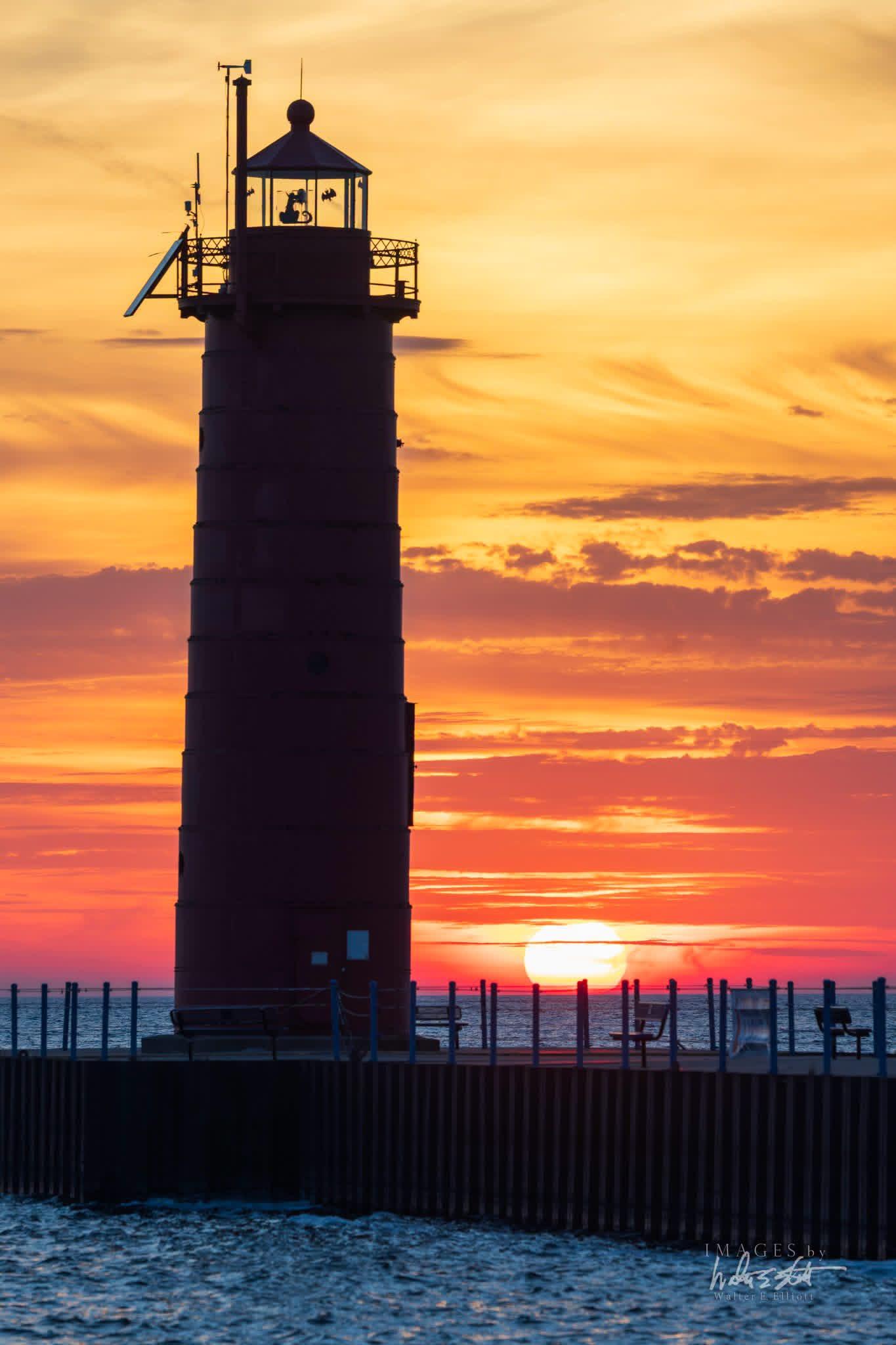 Photo of the sunset on the horizon with a lighthouse on the end of a pier
