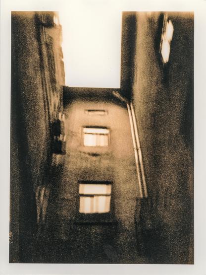 A lith print depicting a courtyard well in the historic center of Lviv, Ukraine. The narrow space is framed by tall, weathered walls  with windows emerging from the shadows. The image was created using multiple exposures, giving the architecture a fragmented, layered appearance. The characteristic lith printing process adds coarse grain, deep blacks, and warm sepia-brown tones, emphasizing the aged, atmospheric character of the courtyard.
