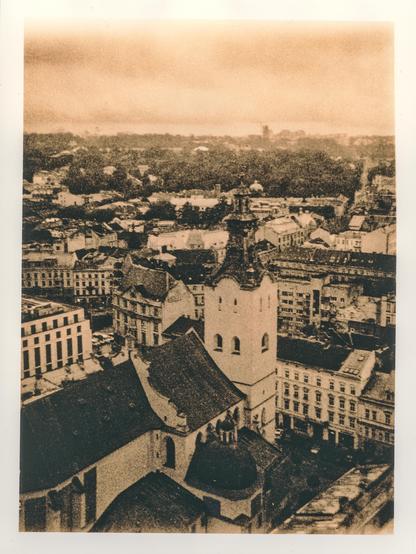 A lith print showing a view over the historic centre of Lviv, Ukraine, photographed from the tower of Lviv Town Hall. The dense cityscape stretches toward the horizon, with layers of historic rooftops, churches, and buildings fading into the distant landscape. The warm sepia-brown tones, coarse grain, and strong contrast give the scene an aged, almost archival character, turning the familiar city into something dreamlike and slightly distant.